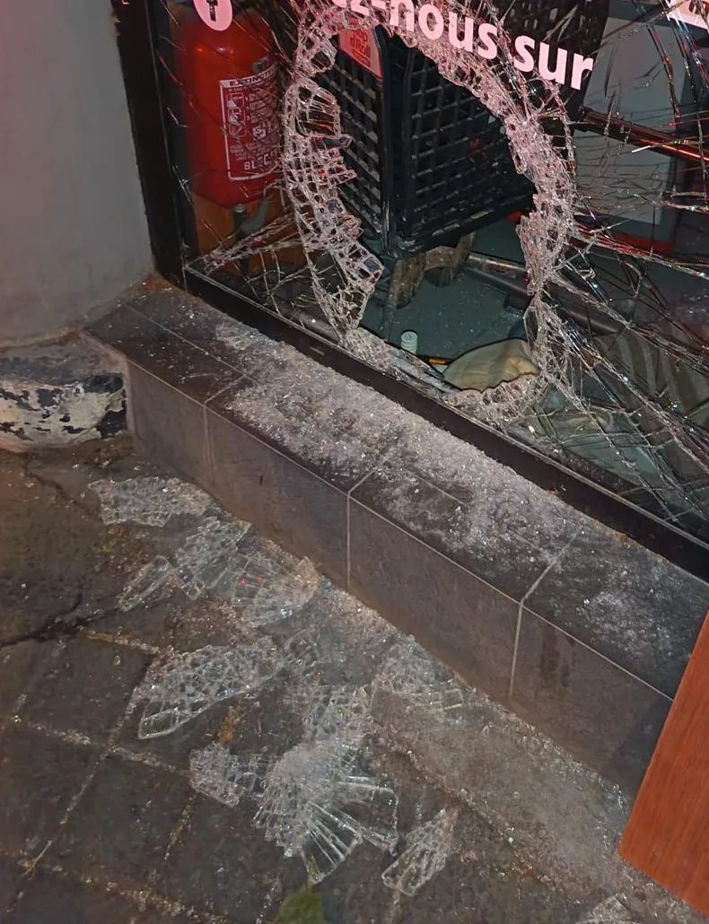 Vitrine de commerce en verre feuilleté fracassée, impact traversant et éclats de verre sur le trottoir